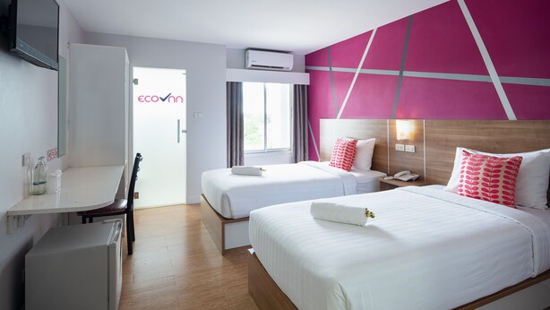 A hotel room with two beds, a desk, a chair, a small fridge, and a window with curtains. - Eco Inn Lite Nakhon Si Thammarat (Nakhon Si Thammarat)