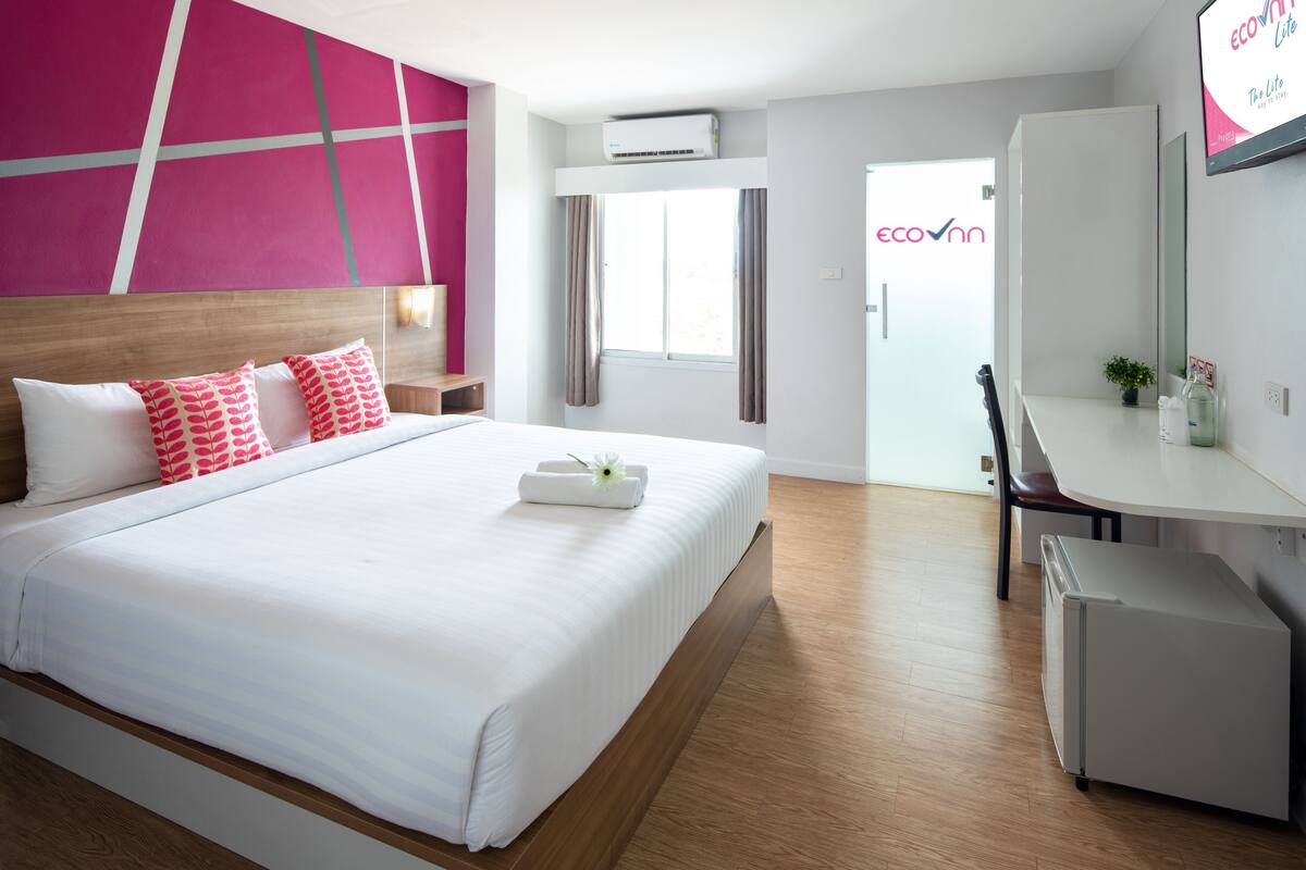 A hotel room with a bed, a desk, a chair, a small refrigerator, and a window with curtains.