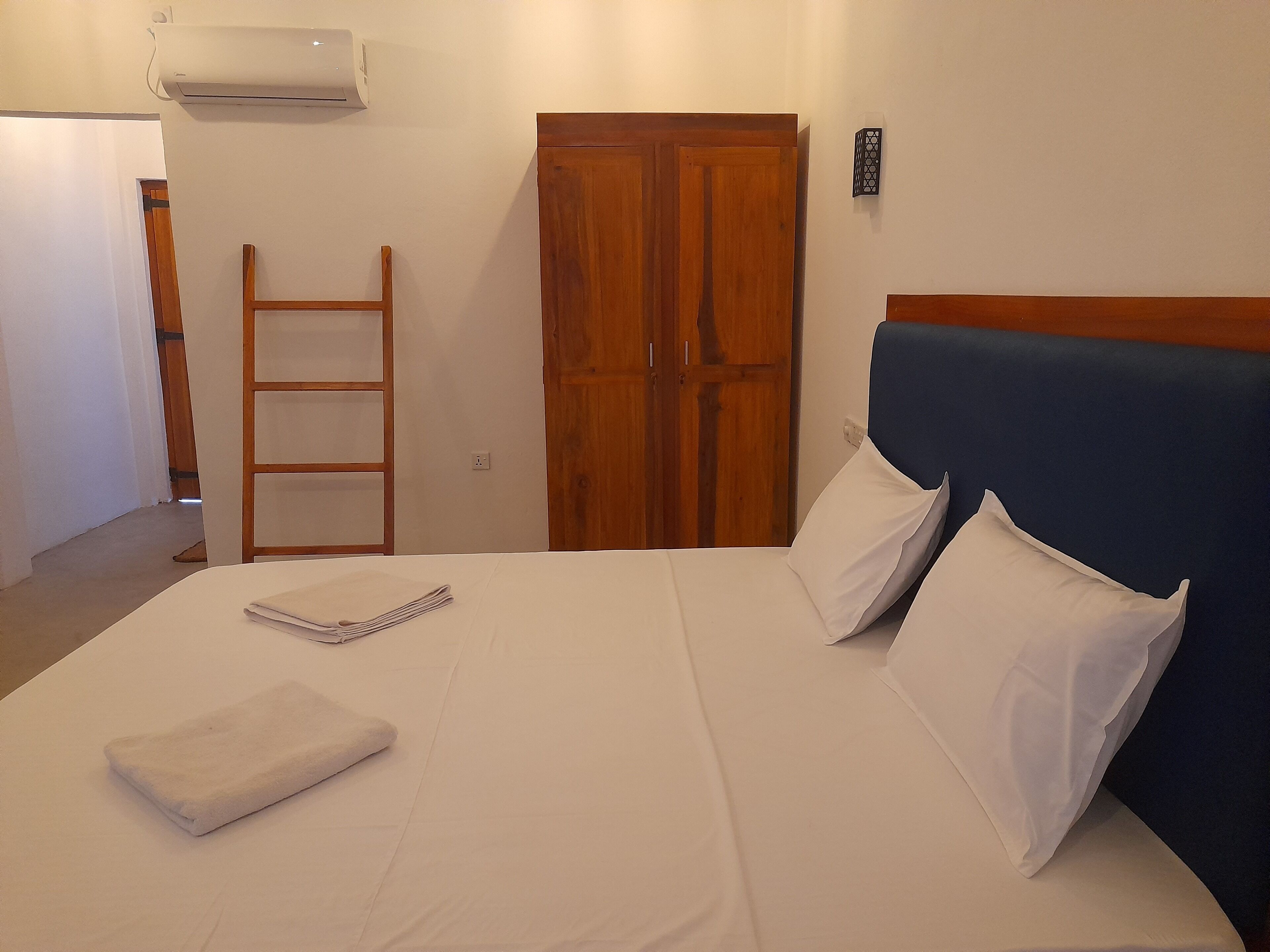 A neatly made bed with white linens, a wooden ladder, and a closed wooden wardrobe.