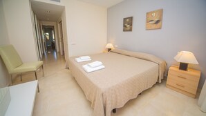 Een slaapkamer met een bed, twee nachtkastjes met lampen, een stoel en een deur naar een andere kamer.