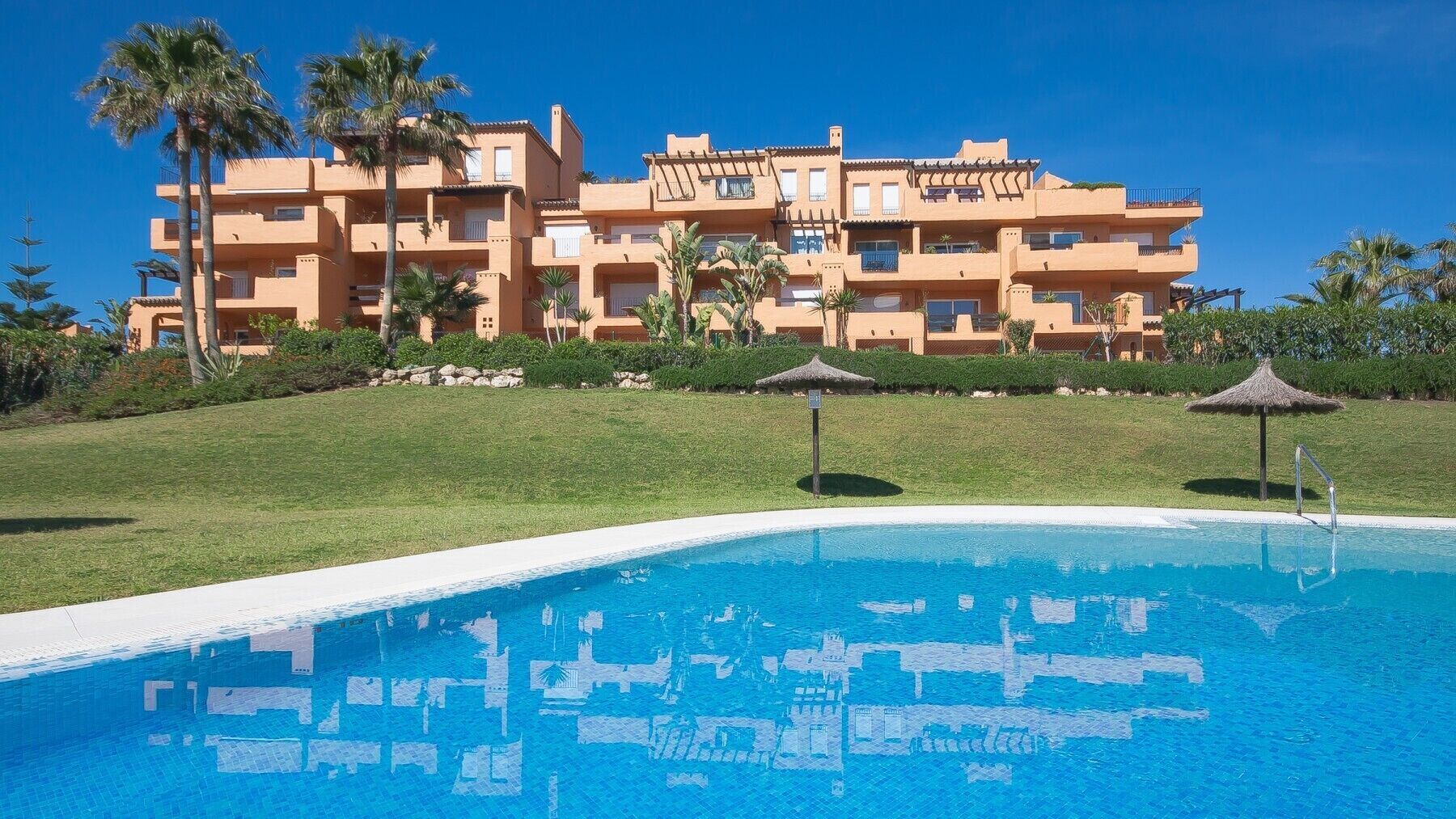 A resort with a swimming pool, palm trees, and a multi-story building with balconies.