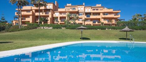 A resort with a swimming pool, palm trees, and a multi-story building with balconies.