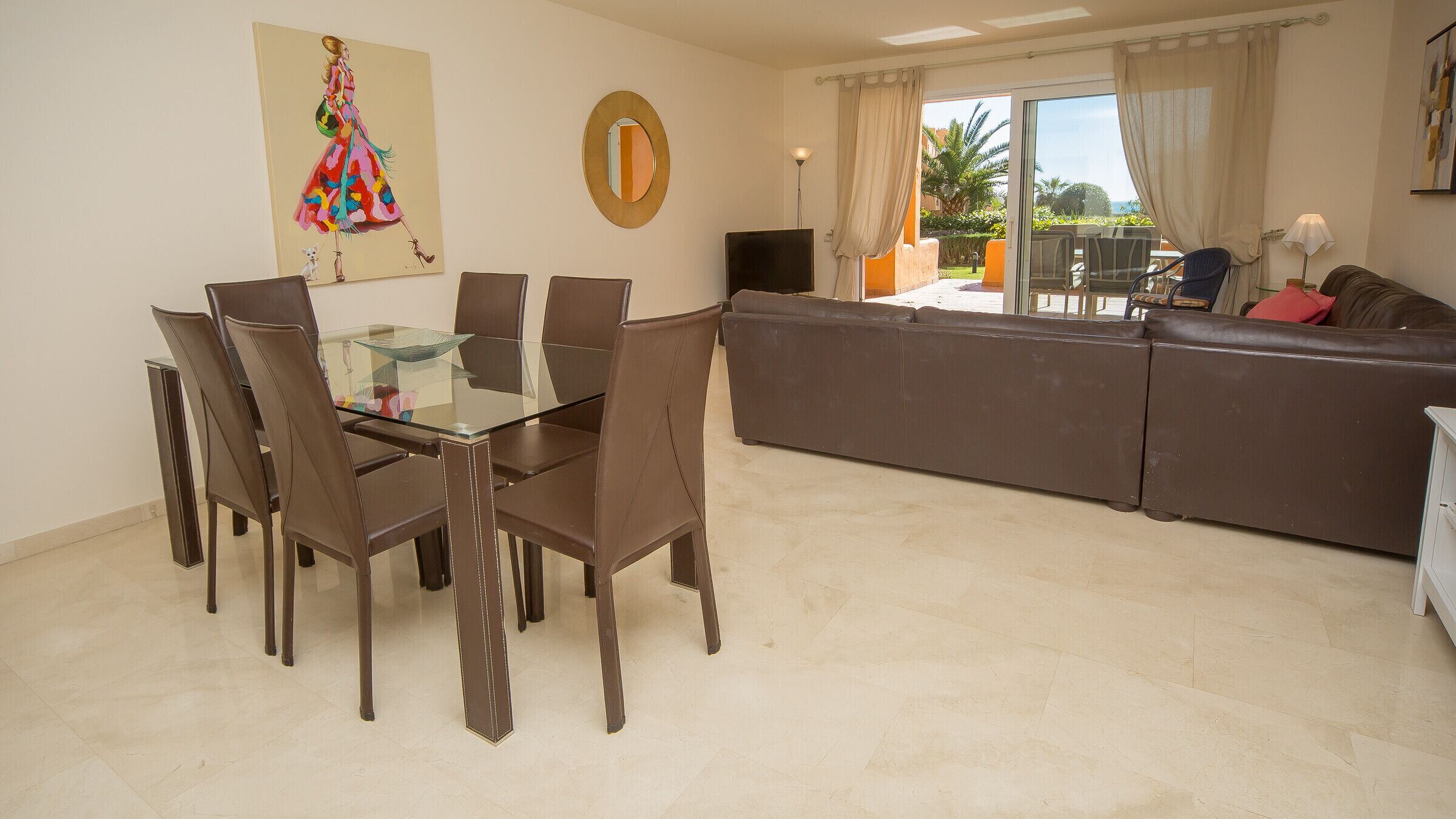 Un comedor con una mesa y sillas de vidrio, un sofá y un cuadro en la pared.