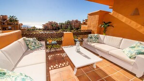 Eine Terrasse mit weißen Sofas, einem Tisch und einem Zierzaun.