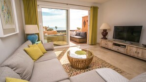 A living room with a sofa, a coffee table, a TV, and a view of the outdoors. - Los Granados de la Duquesa 2022 (Manilva)