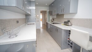 A modern kitchen with grey cabinets, a white countertop, and a stainless steel toaster. - Los Granados de la Duquesa 2022 (Manilva)