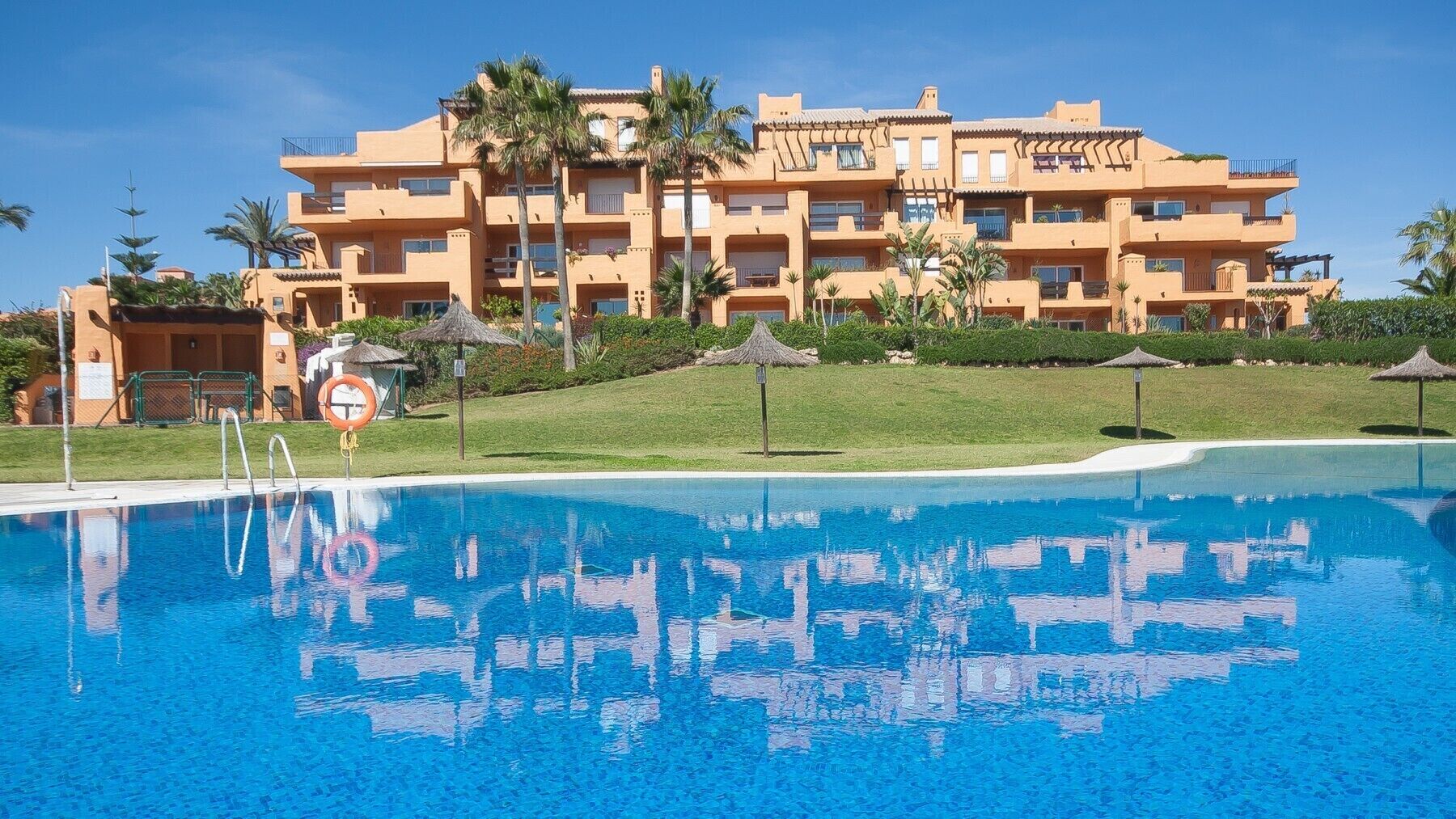 Um hotel com piscina, palmeiras e um céu azul límpido.