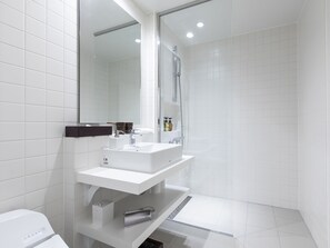 Un baño moderno con azulejos blancos, un espejo grande, un lavamanos y una ducha.