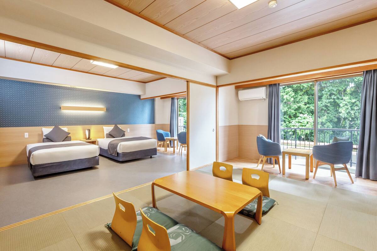 Une chambre d’hôtel moderne dotée d’un grand lit, d’une table à manger et d’un balcon offrant une vue sur la verdure.