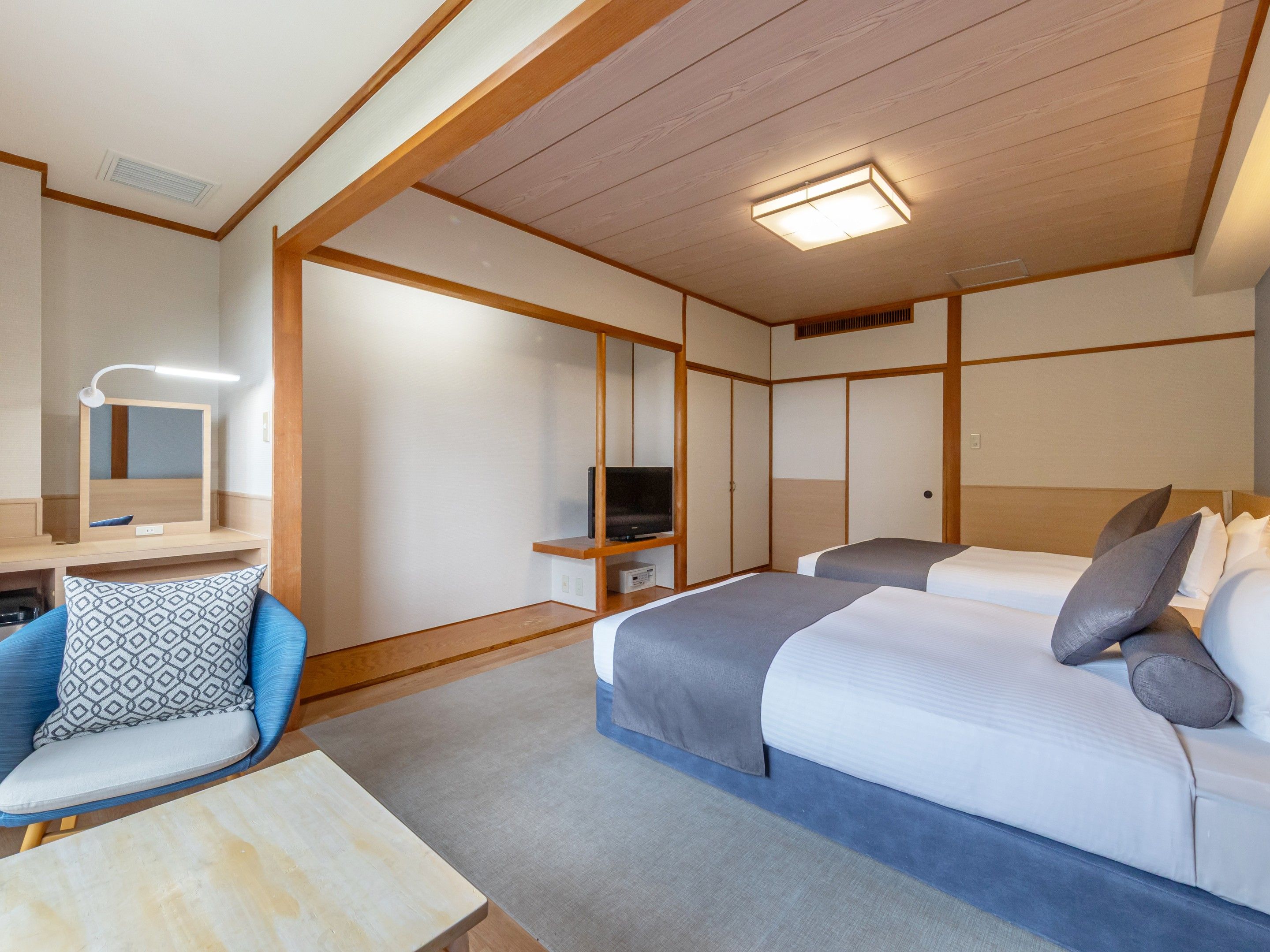 A hotel room with a bed, a desk with a chair, a television, and a mirror.
