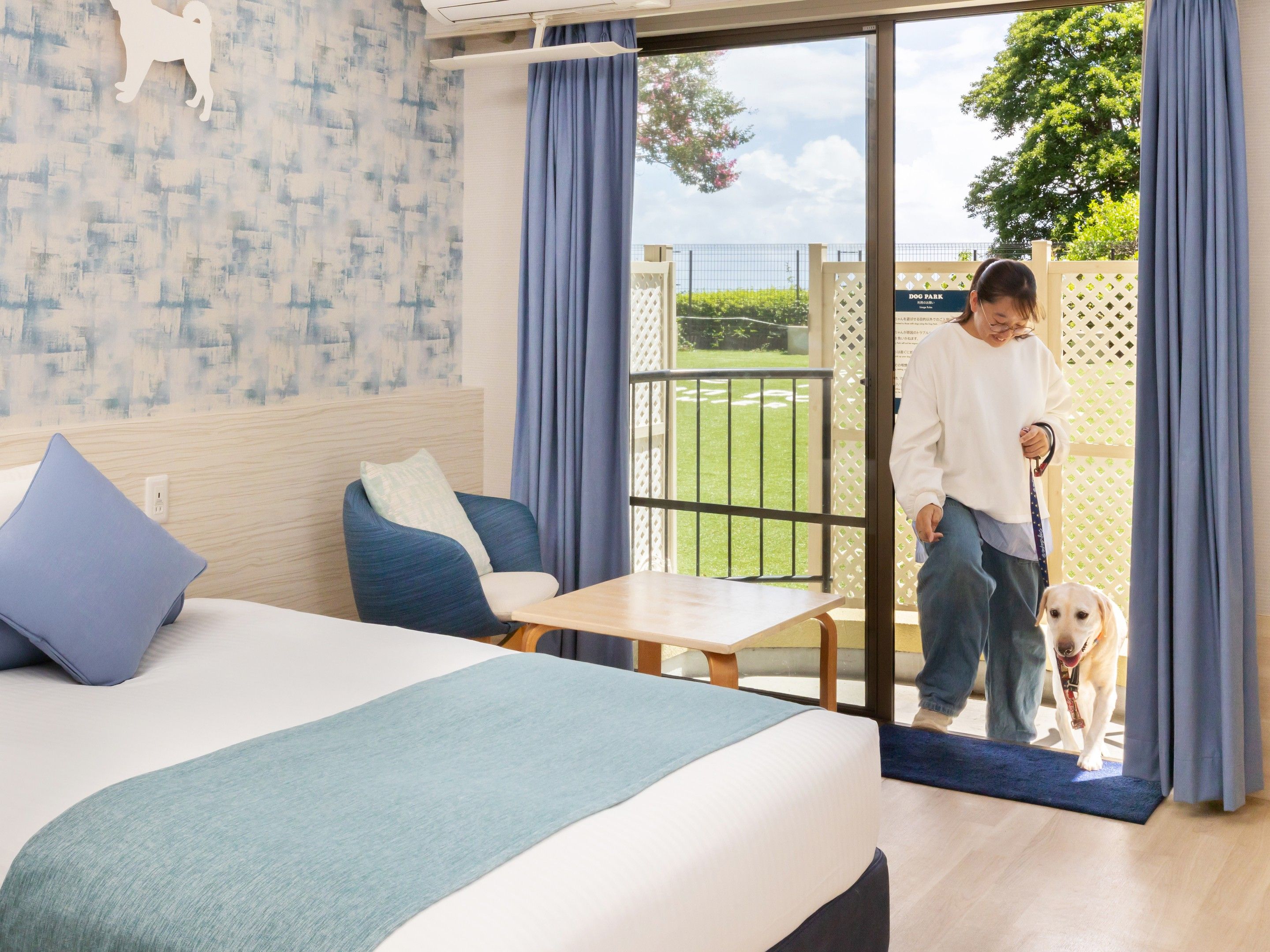 Habitación de hotel con cama, una silla, una mesa y vista a un parque canino por la puerta.