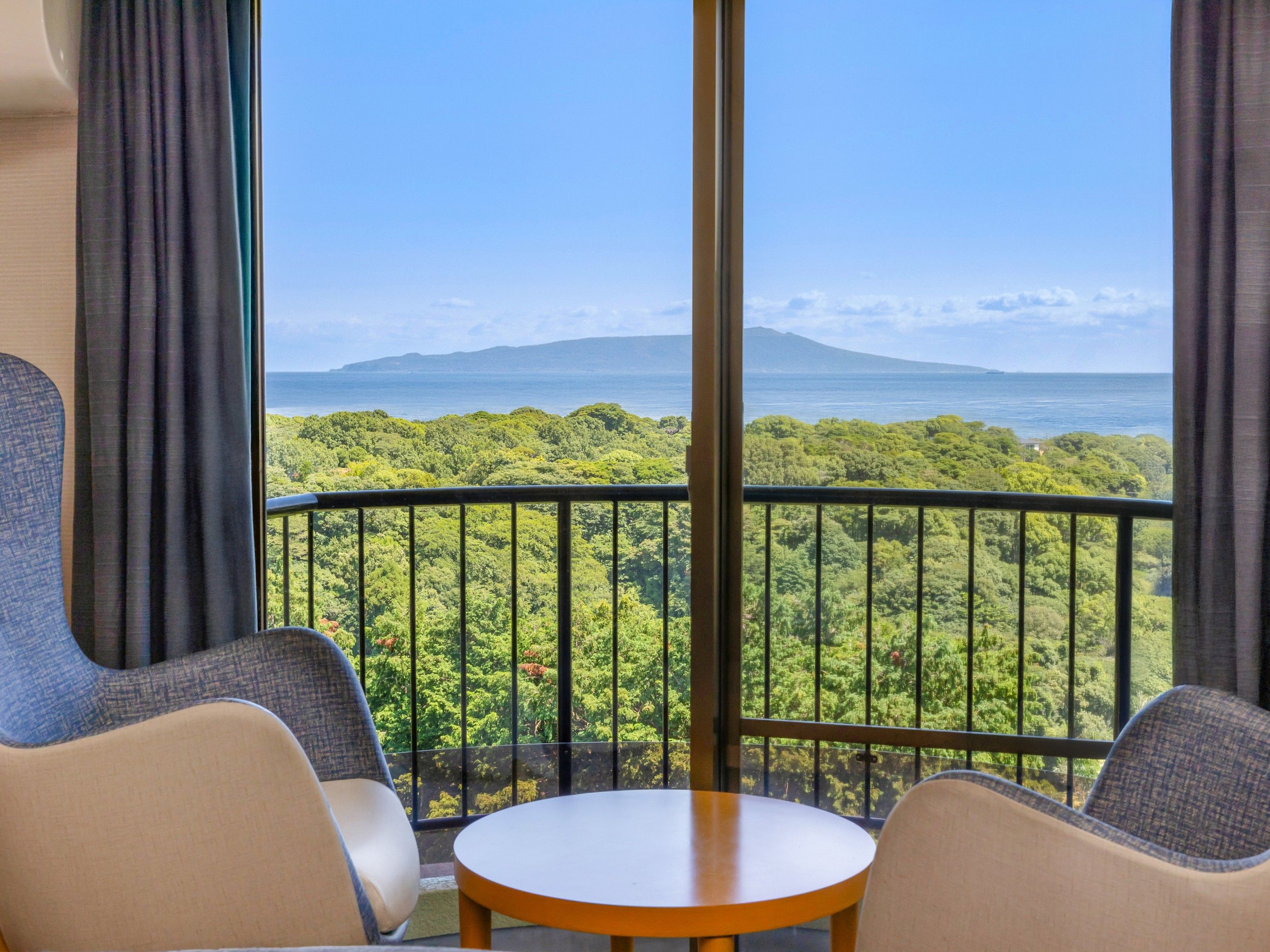 A balcony with a table and two chairs, overlooking a lush landscape and a body of water.