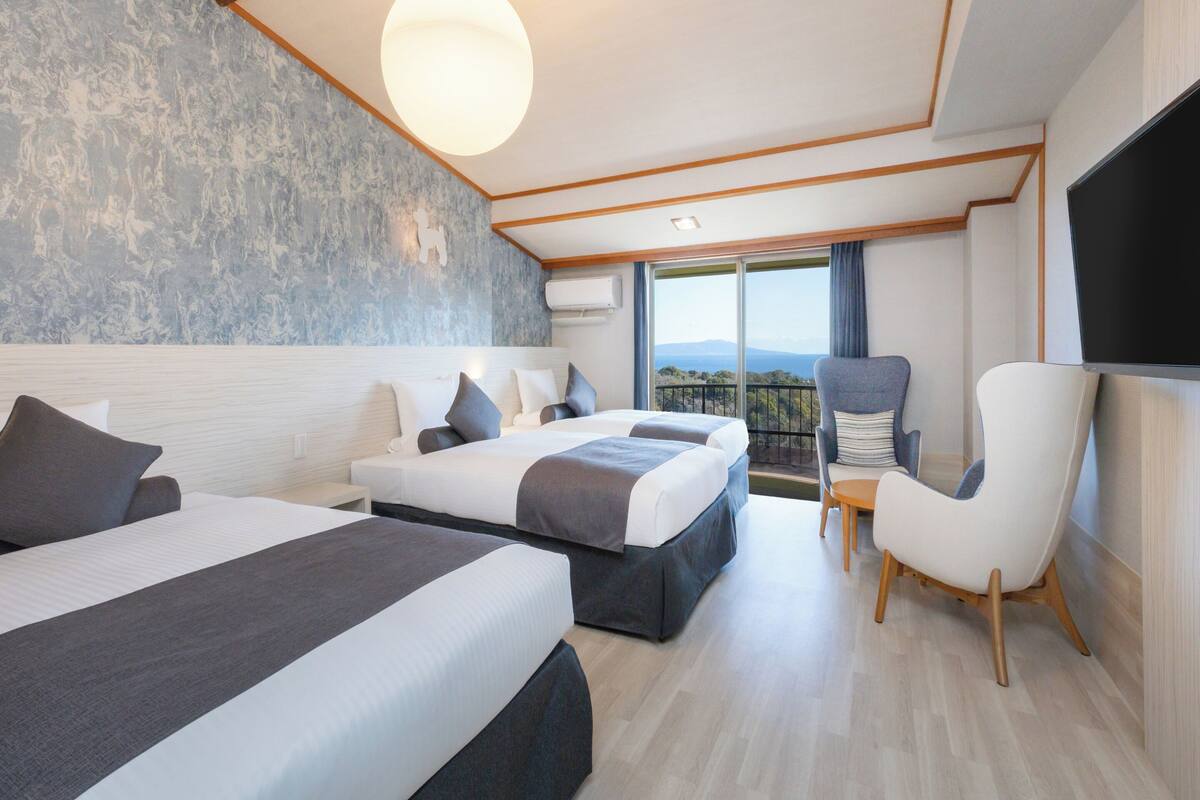 Une chambre d’hôtel moderne avec deux lits, une télévision, un balcon avec vue et un grand luminaire.