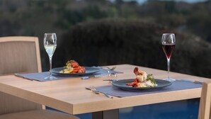 Een eettafel met twee borden eten en twee wijnglazen, voor een pittoresk landschap.