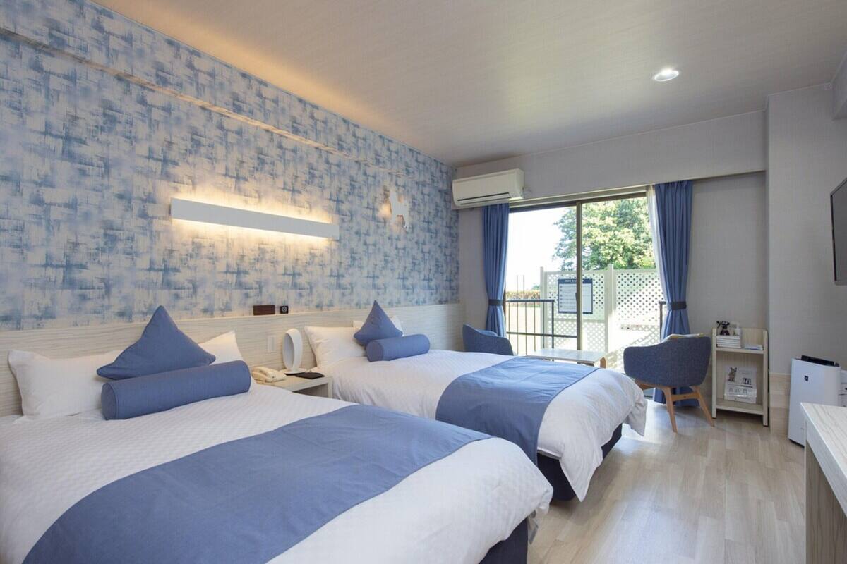 Une chambre d’hôtel avec deux lits, un bureau, une chaise et un balcon avec vue.