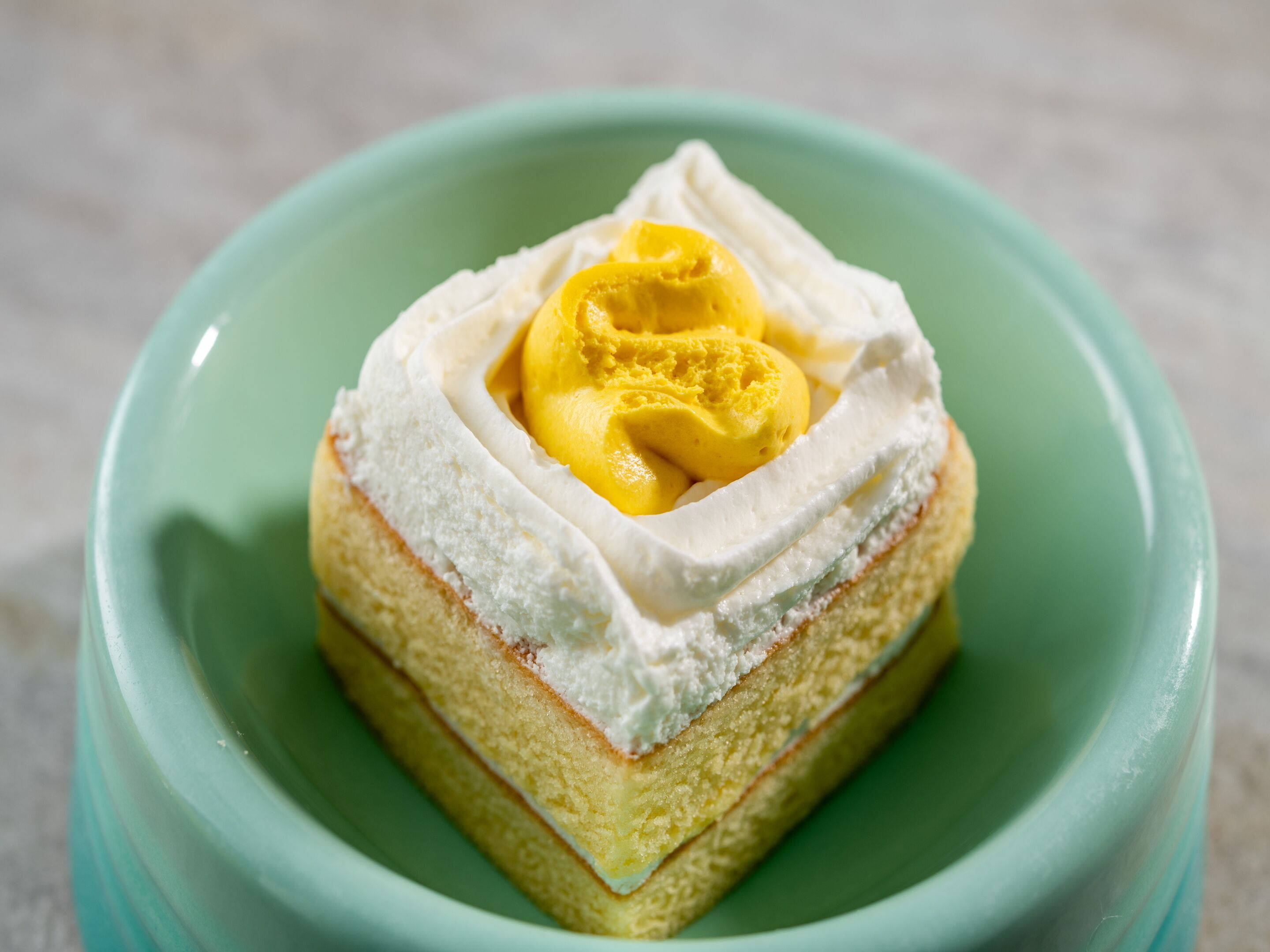 Une part de gâteau à la crème blanche et à la garniture jaune, présentée dans un bol vert.