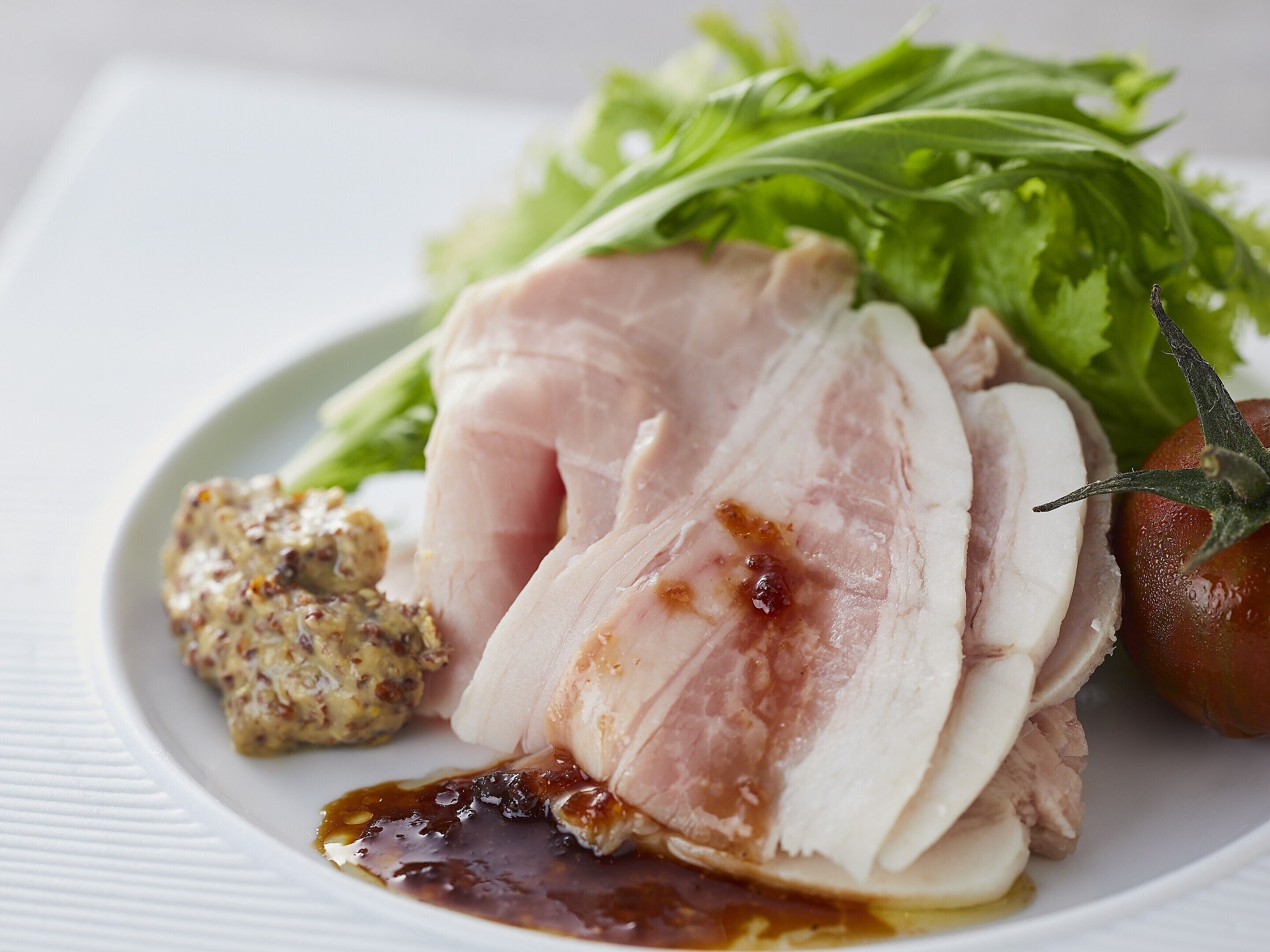A plate with sliced meat, a side of greens, and a dollop of sauce.