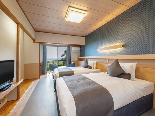 Habitación de hotel con dos camas, televisión, balcón con vistas y diseño moderno.