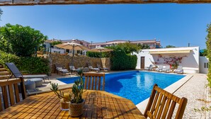 A poolside area with a wooden table, lounge chairs, and a stone wall.