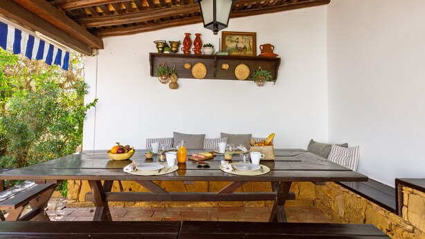A wooden table set for breakfast with plates, cups, and a fruit bowl.