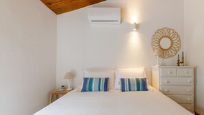 A bedroom with a bed, a nightstand, a dresser, an air conditioning unit, and a decorative mirror.
