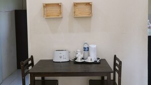 A dining area with a table, chairs, a toaster, a kettle, and two wooden wall-mounted shelves. - Kuala Mengalong Cottage (Sipitang)