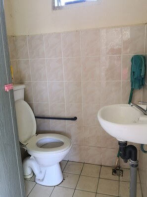 A bathroom with a toilet, a sink, and a mop leaning against the wall.