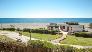 Um imóvel costeiro com um pátio pavimentado, um pequeno edifício com telhado verde e vista para o mar.