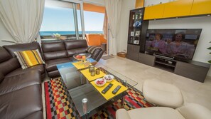 Ein modernes Wohnzimmer mit einem Glastisch, einer Ledersofa und einem Fernseher auf einem Standfuß.