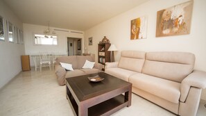 Una sala de estar con un sofá color beige, una mesa de centro y un comedor con una mesa y sillas blancas.