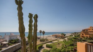 A coastal view with a beach, cacti, and Mediterranean-style buildings.