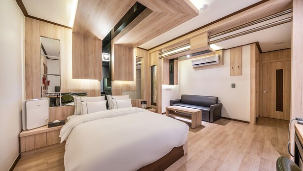 Quarto de hotel moderno com uma cama grande, uma mesa, um sofá e um espelho.