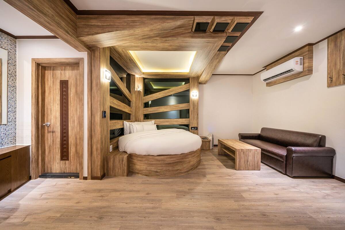 Ein modernes Schlafzimmer mit einem gewölbten Bett, Holzbalkendecke, einer eingebauten Sitzbank und einem braunen Ledersofa.