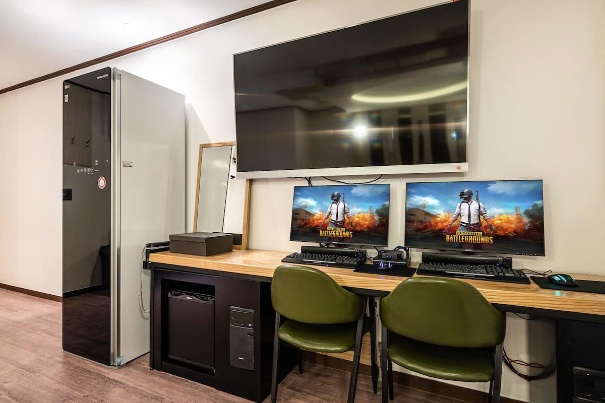 Ein kleiner Büroraum mit Schreibtisch, zwei Monitoren, einer Tastatur und einem grünen Stuhl.