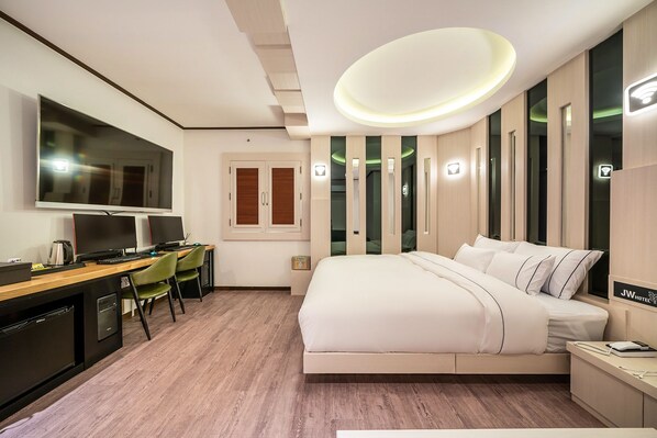 Una habitación de hotel moderna con una cama grande, un escritorio con dos sillas, un televisor y un armario empotrado.