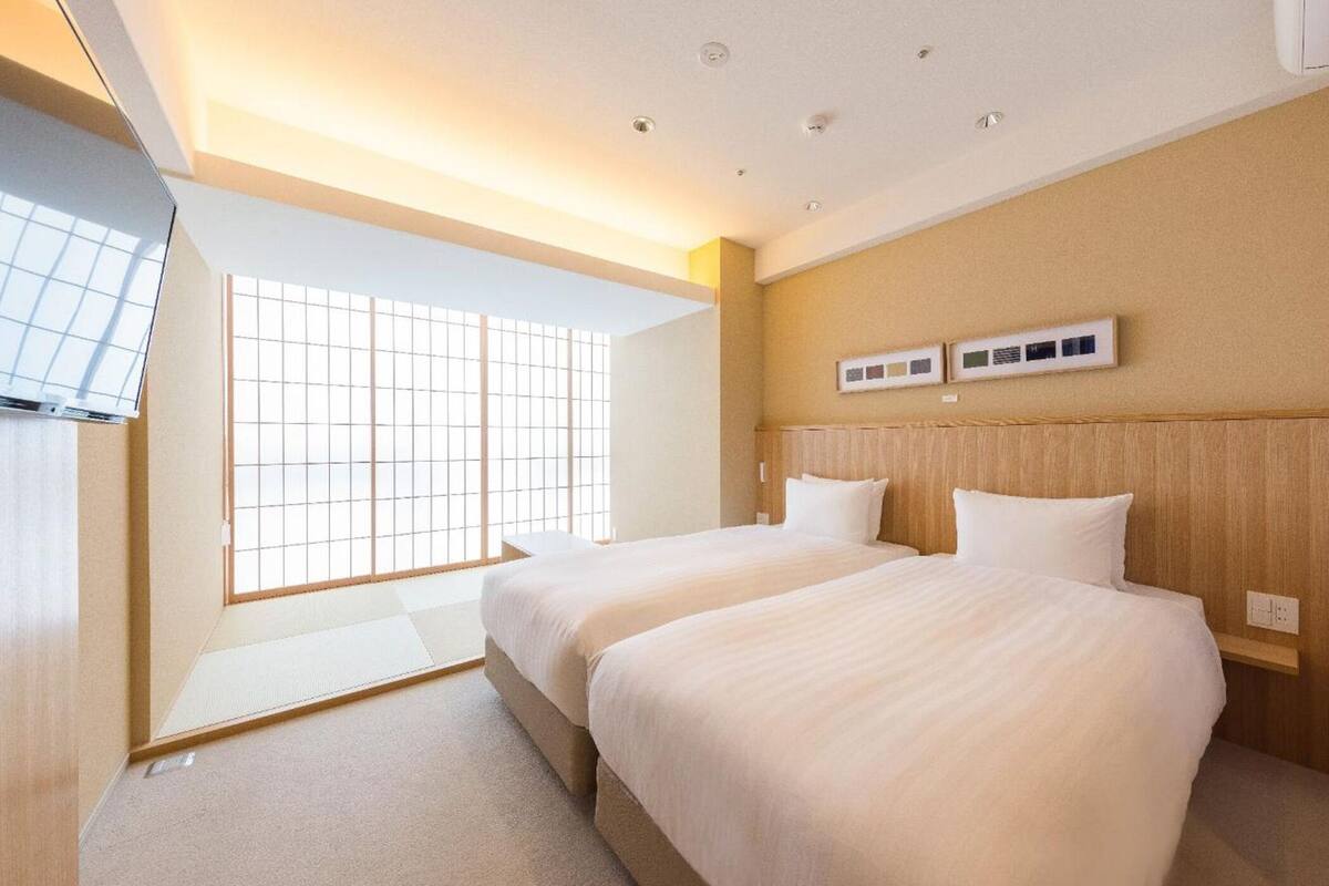 A hotel room with two beds, a large window, and a wall-mounted TV.