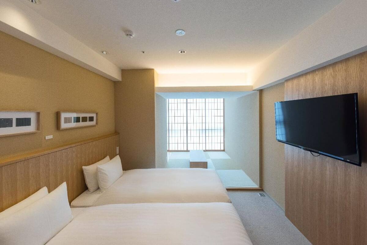 A hotel room with two beds, a television, and a window with a view.