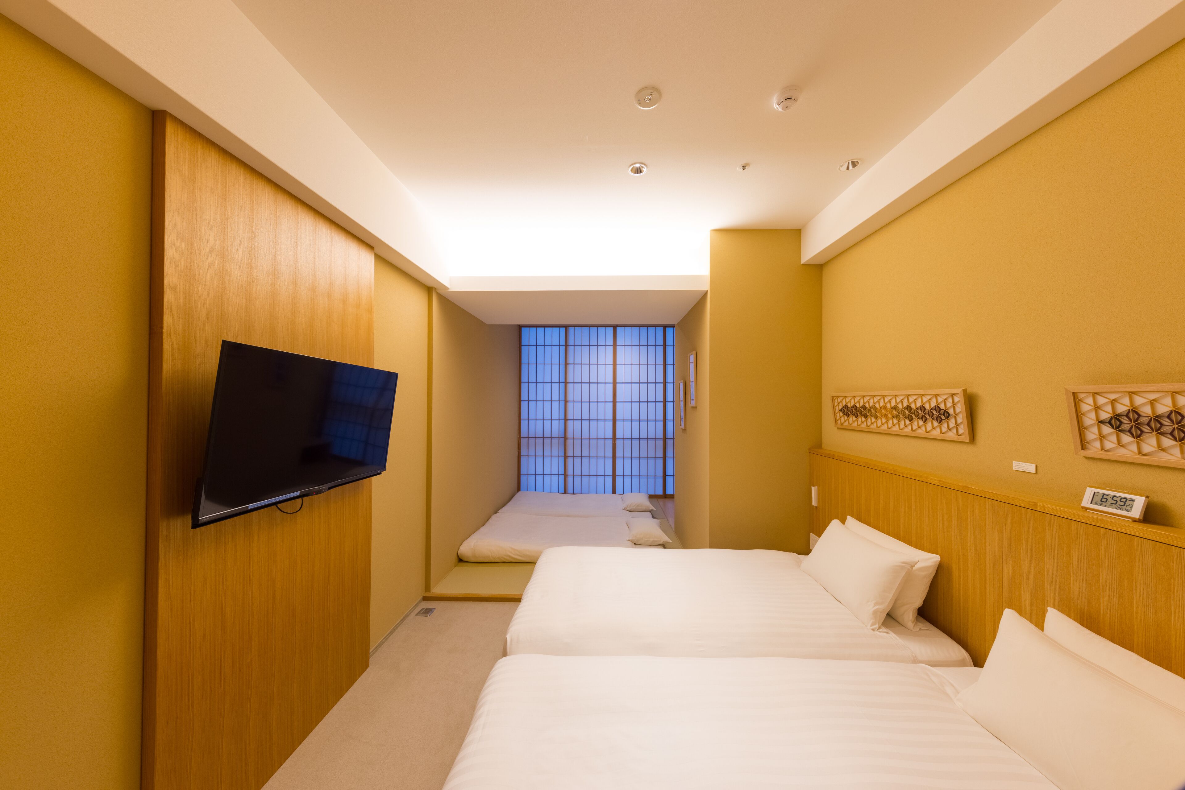 Ein Hotelzimmer mit zwei Betten, einem an der Wand befestigten Fernseher, einem Fenster mit Aussicht und einer Wanduhr.