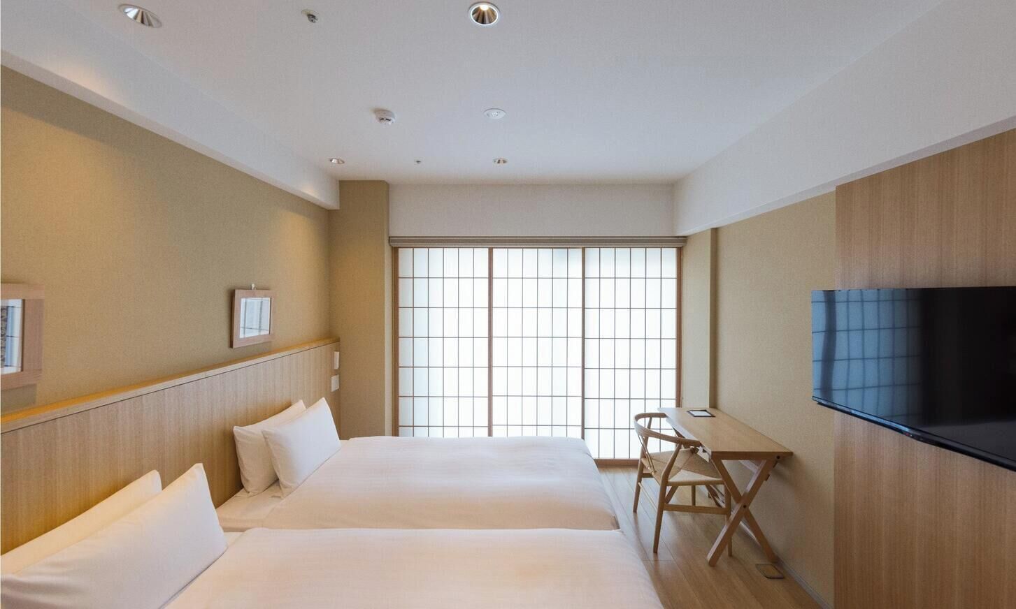 A hotel room with two beds, a desk, a chair, a TV, and a large window.