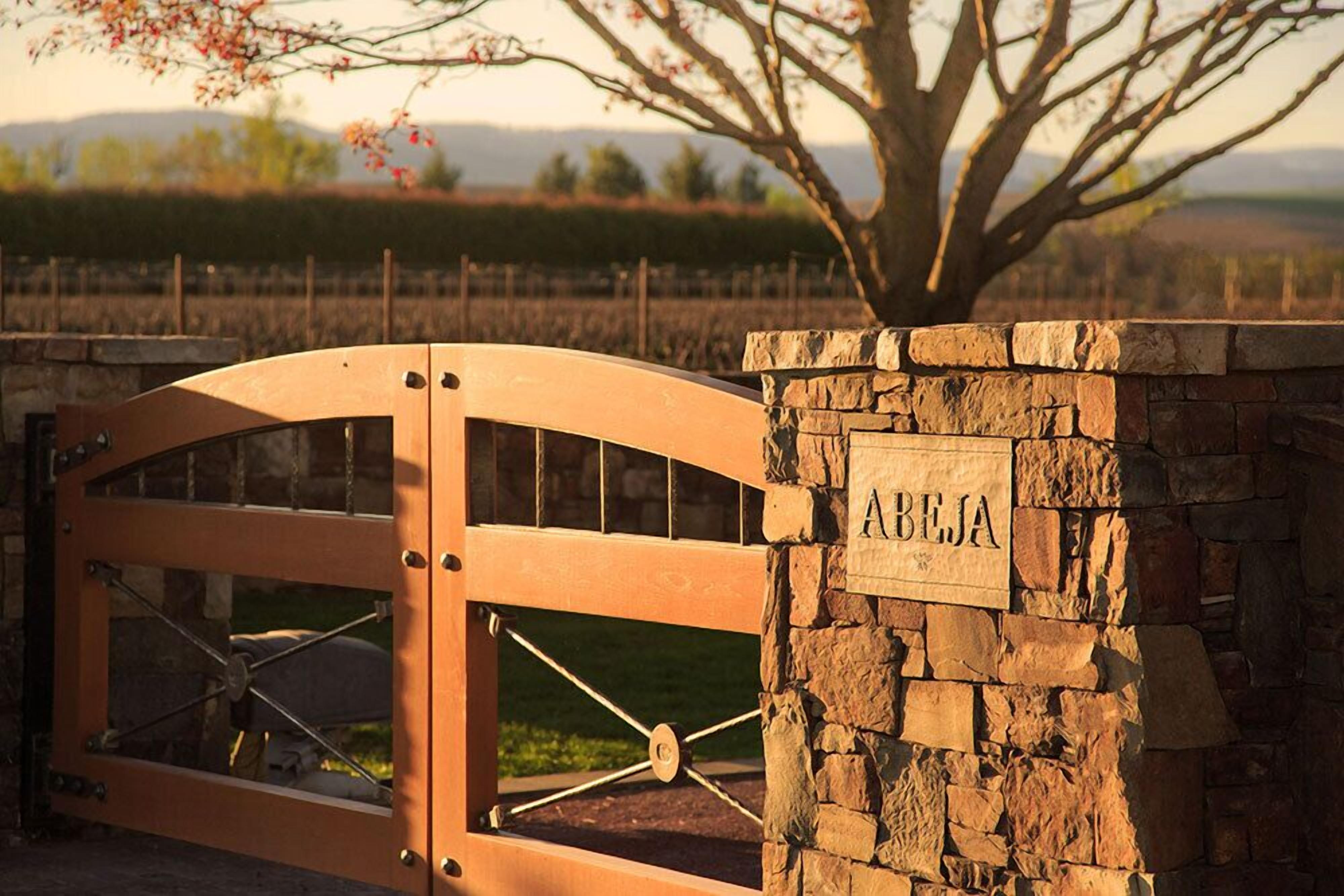 A stone wall with a sign that reads "ABELJA" and a wooden gate with a metal mechanism.