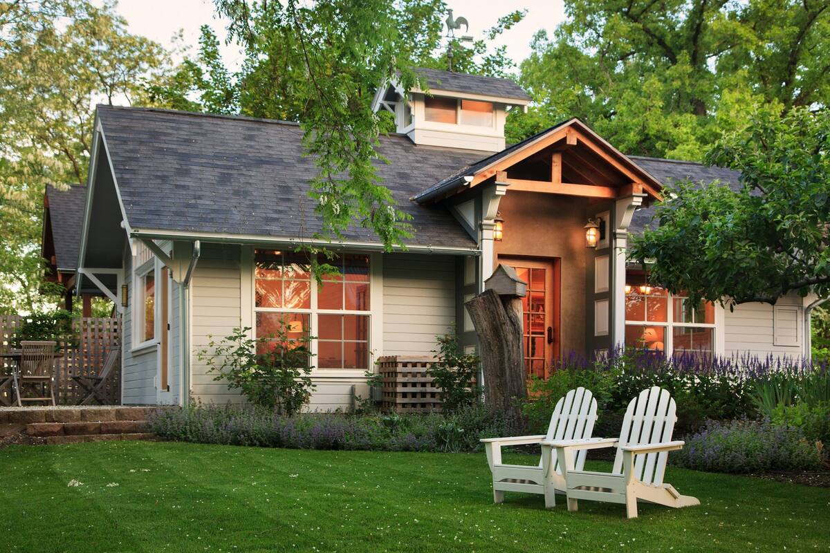 A house with a porch, two Adirondack chairs, and a well-maintained lawn.