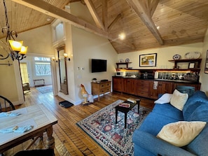 A spacious living room with a blue sofa, wooden flooring, a dining area with a table, and a kitchen with wooden cabinets and a TV.