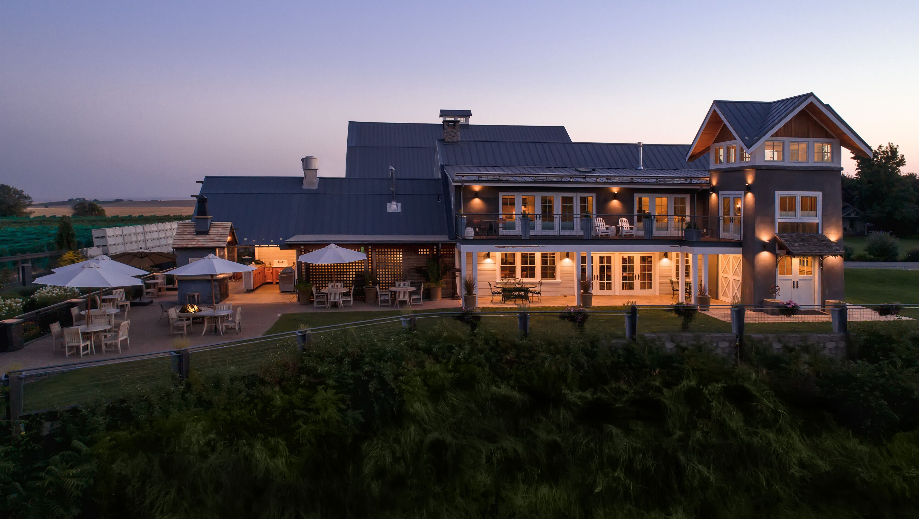 A two-story house with a large patio area, outdoor seating, and a well-lit entrance.