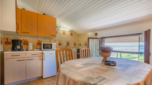 Una cucina compatta con mobili in legno, un forno a microonde e un piccolo frigorifero. C'è un tavolo da pranzo con una tovaglia fantasia e una pianta in vaso.