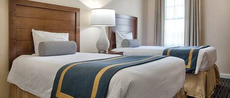 A hotel room with two beds, a wooden headboard, a lamp, and a window with curtains.