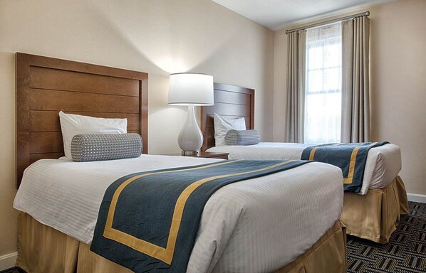 A hotel room with two beds, a wooden headboard, a lamp, and a window with curtains.