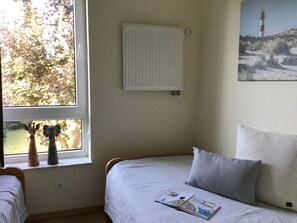 A bedroom with a bed, a window with a view of trees, a radiator, and a painting of a lighthouse.