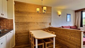 Eine kleine Küche mit Holzvertäfelung, einem Esstisch mit Stühlen, einer eingebauten Bank und einem Fenster mit Vorhängen.