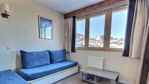 Ein Zimmer mit einem blauen Sofa, einem kleinen Tisch und einem Fenster mit Bergblick.