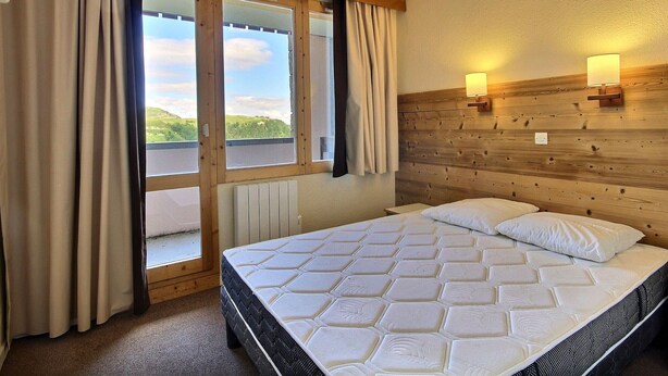 Ein Hotelzimmer mit einem großen Bett, einem Holzkopfende, zwei Wandleuchten und Blick auf eine grüne Landschaft durch eine Schiebetür.